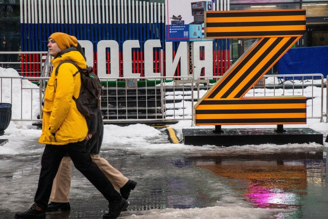 Moscow, Russia. 24th of December, 2022. Young people walk on Industry Square against the background of the sign Z in support of Russian Armed Forces in the colors of the St. George ribbon and the inscription