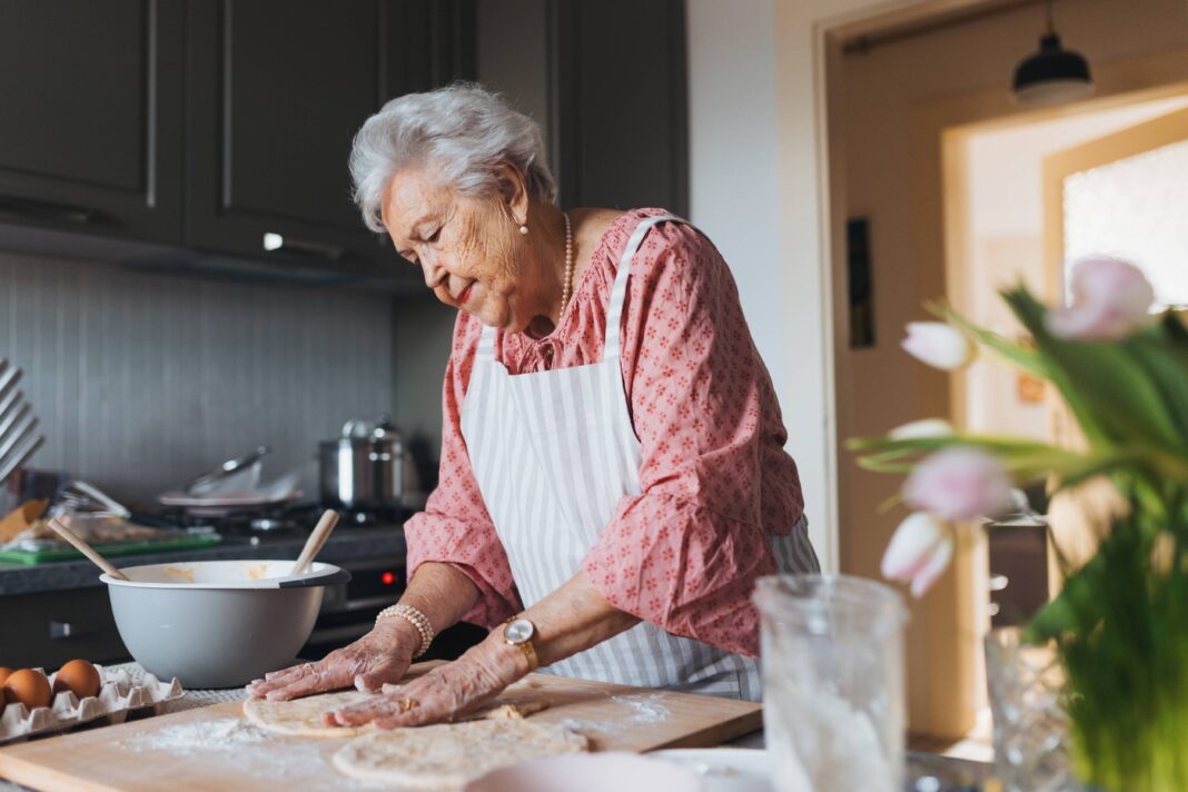 Senior woman preparing traditional easter meals for family, kneading dough for easter cross buns. Recreating family reci